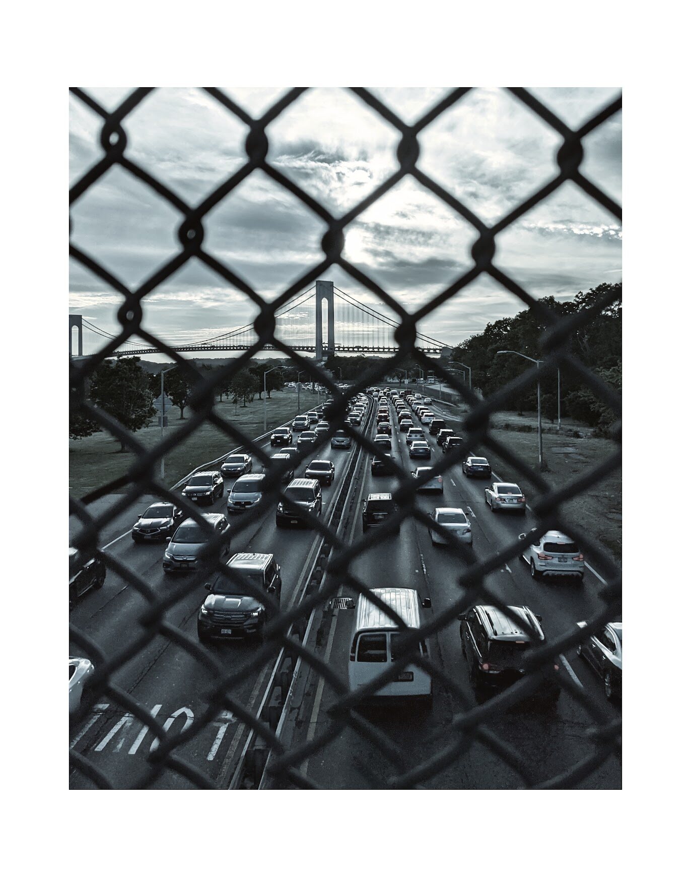 Black and white highway traffic seen through a chain-link fence