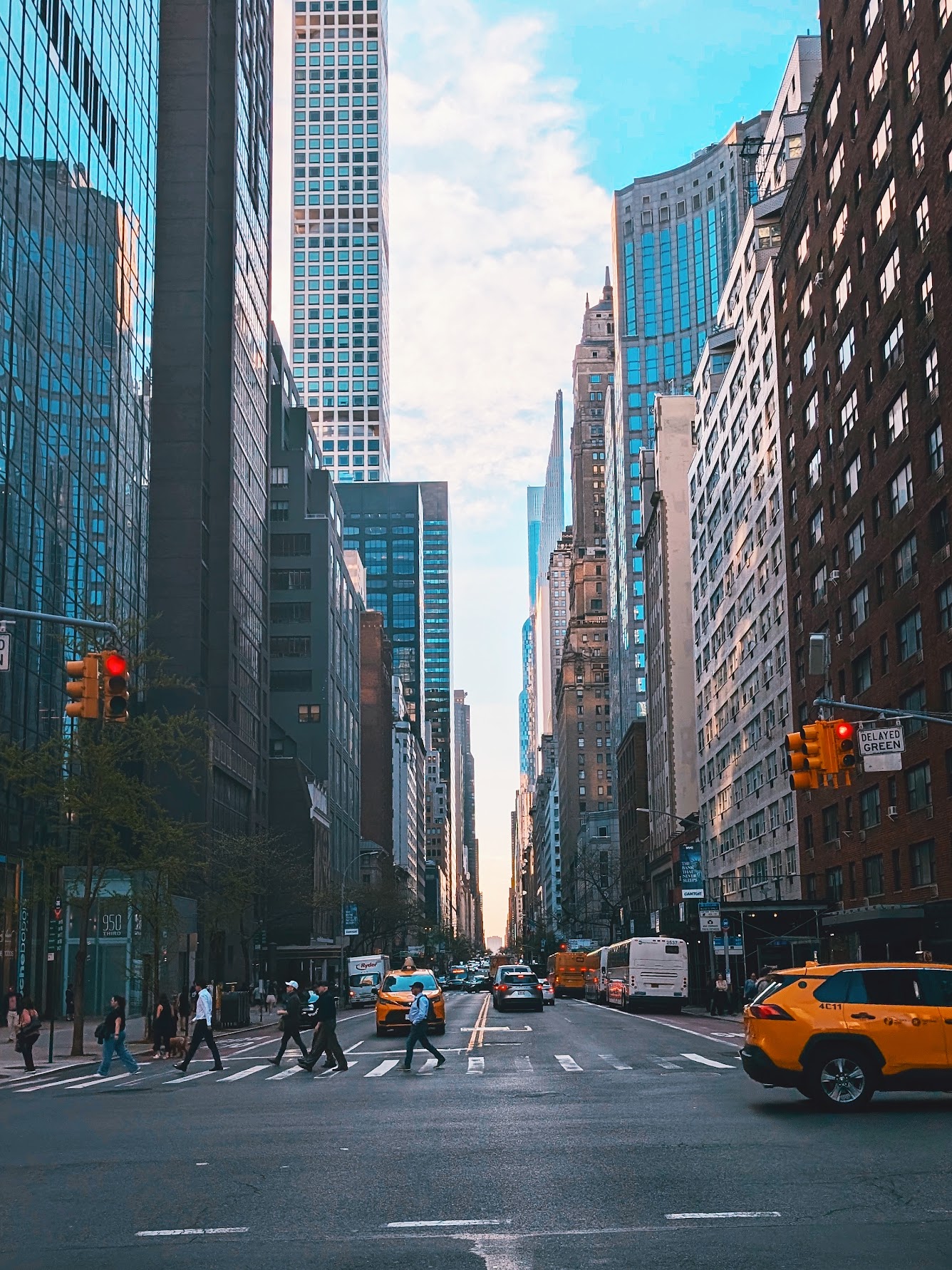 Yellow taxis and pedestrians crossing a Manhattan avenue lined with skyscrapers