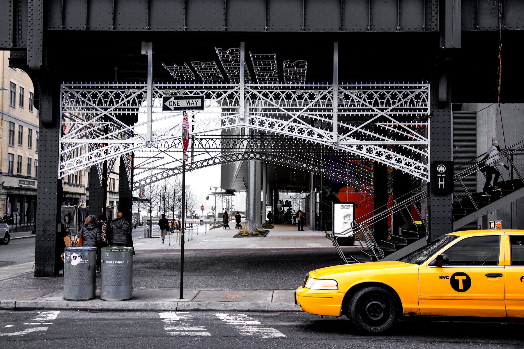 Black and white elevated train tracks with a yellow taxi below