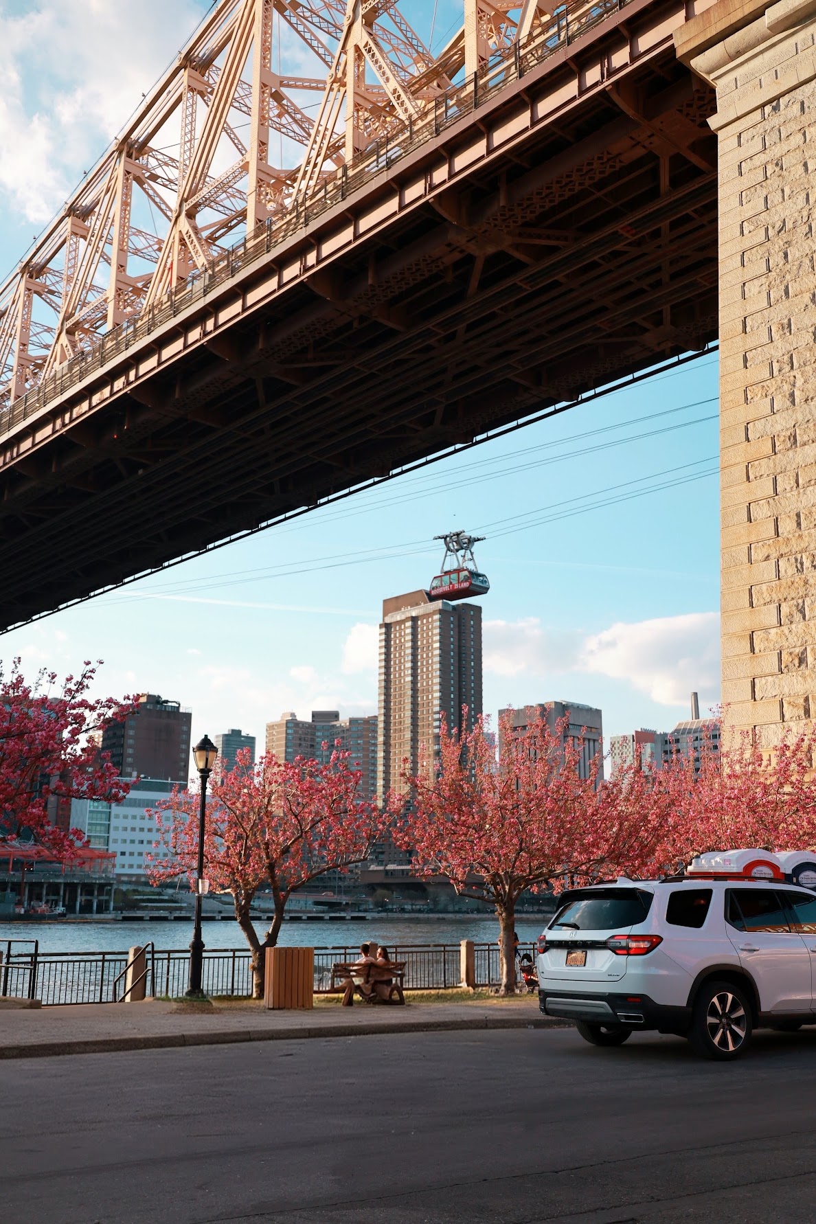 Roosevelt Island tram passing under the Queensboro Bridge with cherry blossoms in bloom